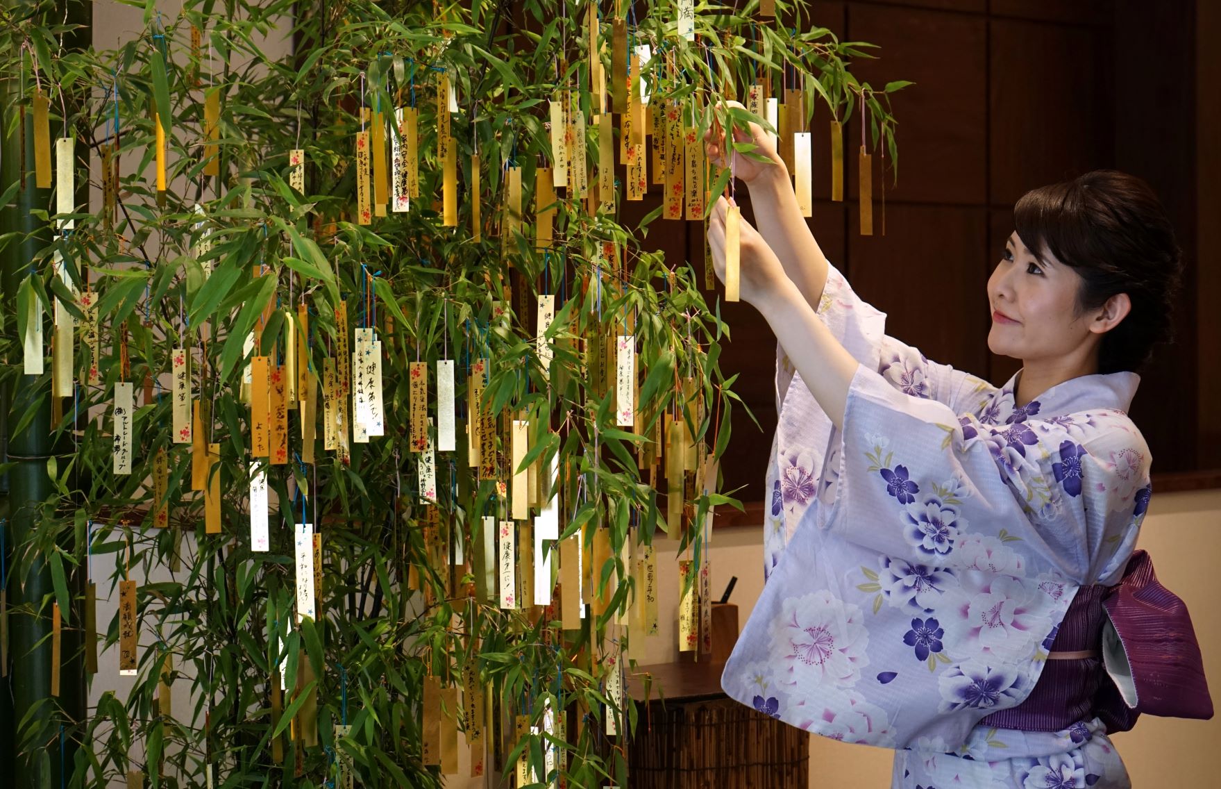  A jewelry store employee hangs a gold leaf strip wishing card onto a bamboo decoration during the annual celebration of “Tanabata” in Tokyo on July 4, 2018. (File photo: AFP)