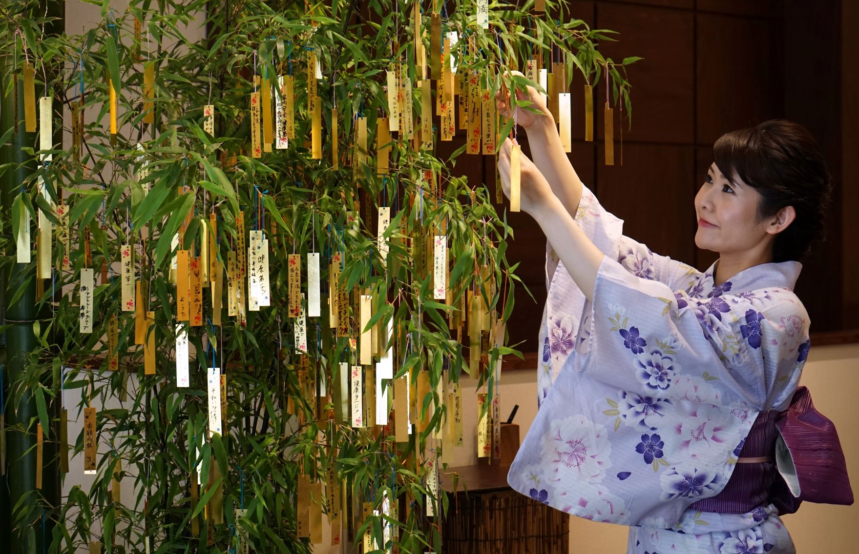 A jewelry store employee hangs a gold leaf strip wishing card onto a bamboo decoration during the annual celebration of “Tanabata” in Tokyo on July 4, 2018. (File photo: AFP)