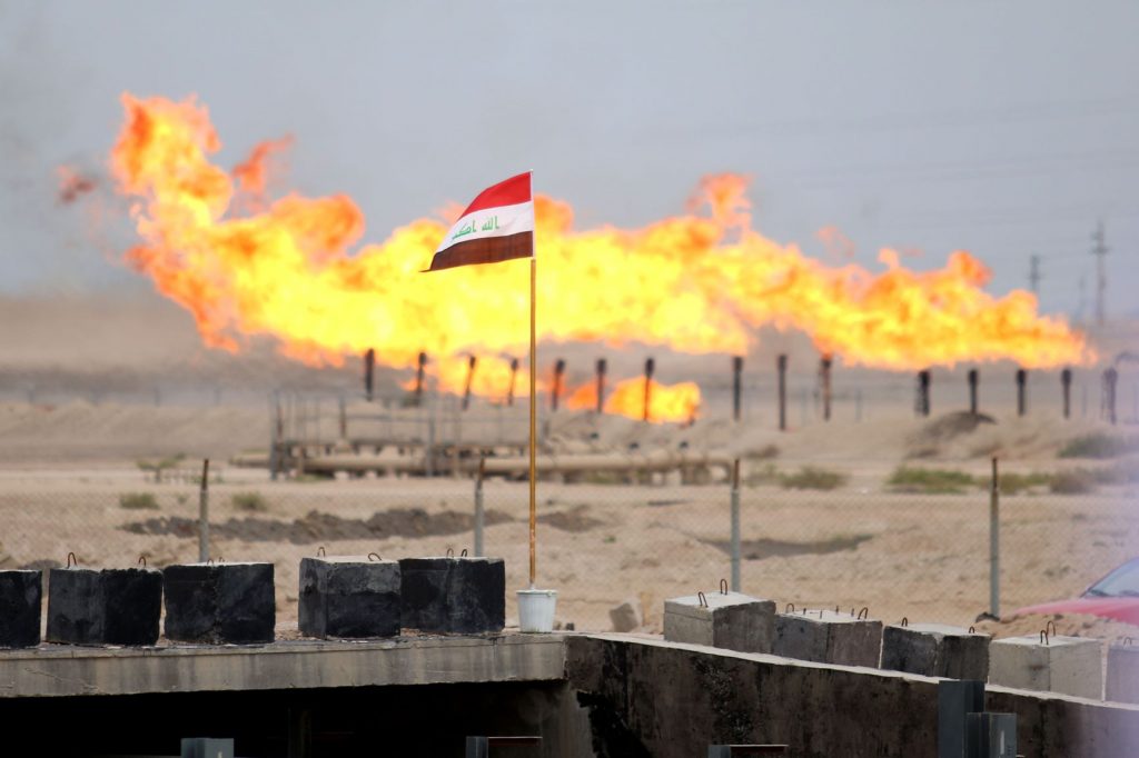 An Iraqi national flag in front of excess gas as its being burnt off, at a pipeline in the newly opened section of the oil refinery of Zubair, southwest of Basra, on March 3, 2016. (AFP)