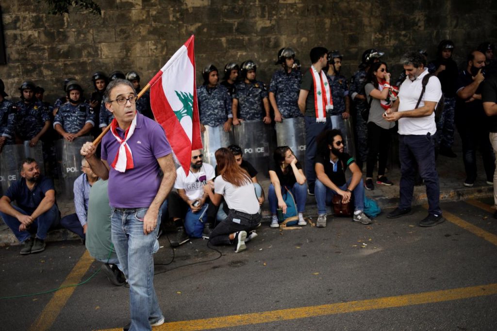 A flag-bearing protester stands in front of police outside the Ministry of Foreign Affairs and Emigrants in Beirut. (Reuters)