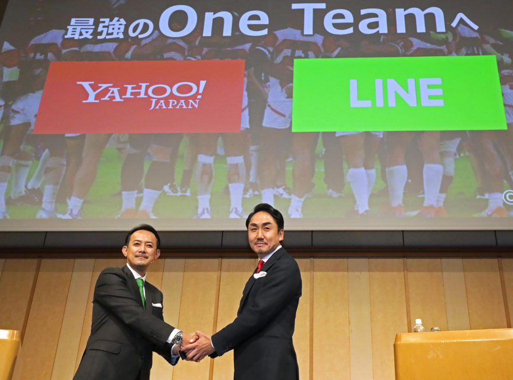 Kentaro Kawabe (L), CEO and president of Z Holdings and Takeshi Idezawa (R), CEO and president of LINE shake hands during a joint press conference in Tokyo on November 18, 2019. (Jiji Press / AFP)