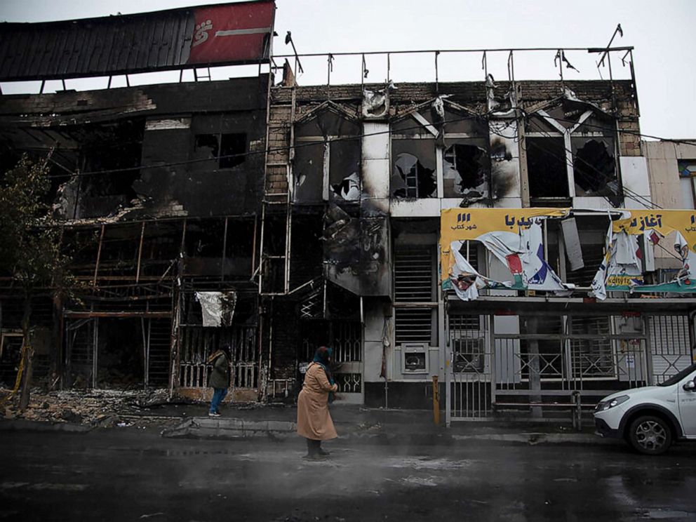 People walk past burnt-out buildings following protests after a rise in gasoline prices, in the city of Karaj, west of Tehran. (AP Photo)