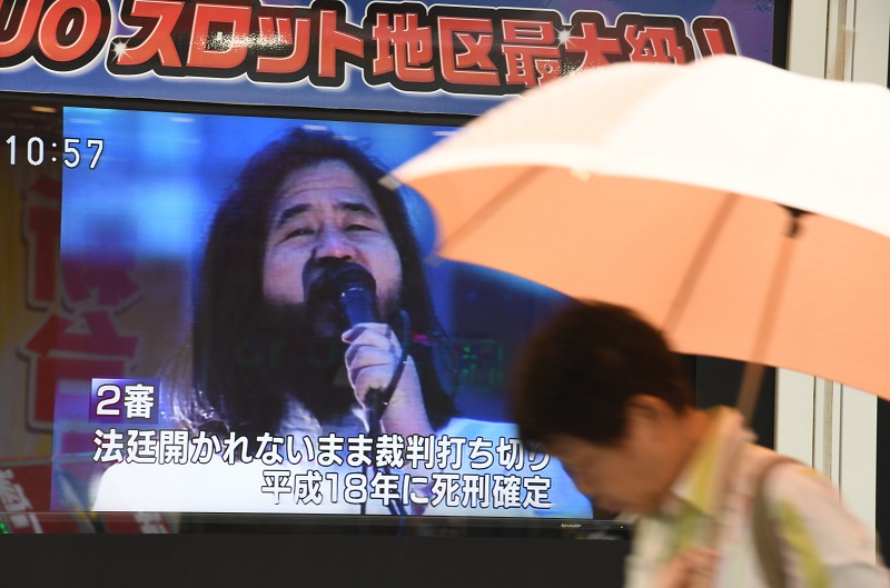 A pedestrian walks past a TV screen flashing news about Shoko Asahara, leader of the Aum Shinrikyo cult, after the execution of six other members of the Aum Supreme Truth doomsday cult, in Tokyo on July 26, 2018. (AFP/file)
