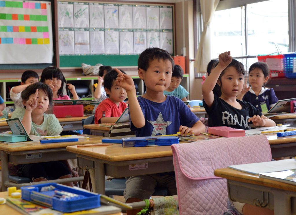 Six-year-old Japanese elementary student Seishi Nishida (C) raises his hand along with classmates at school in Tokyo on June 11, 2013. (AFP)