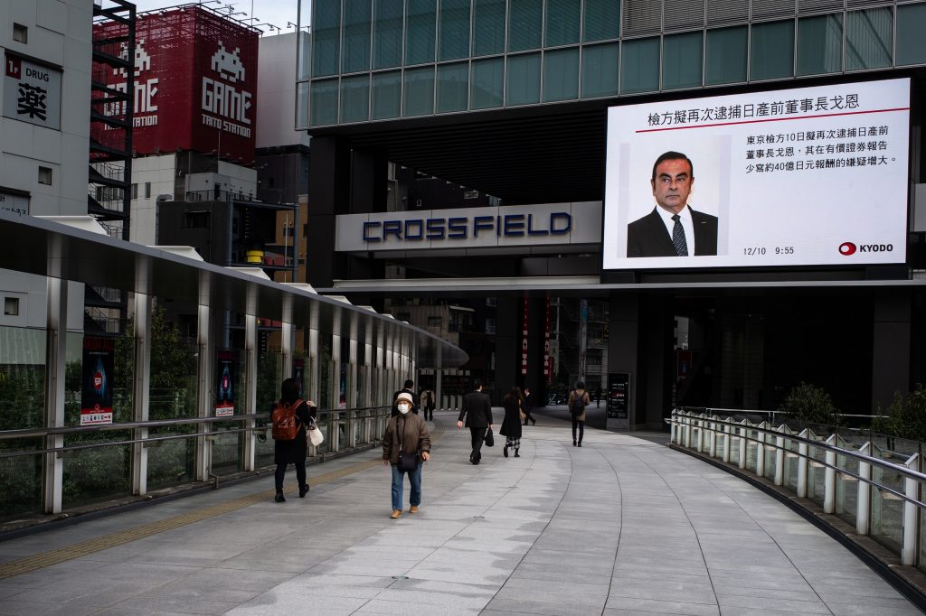 Pedestrians walk past a television screen showing a news program featuring former Nissan chief Carlos Ghosn in Tokyo on December 10, 2018. (AFP)