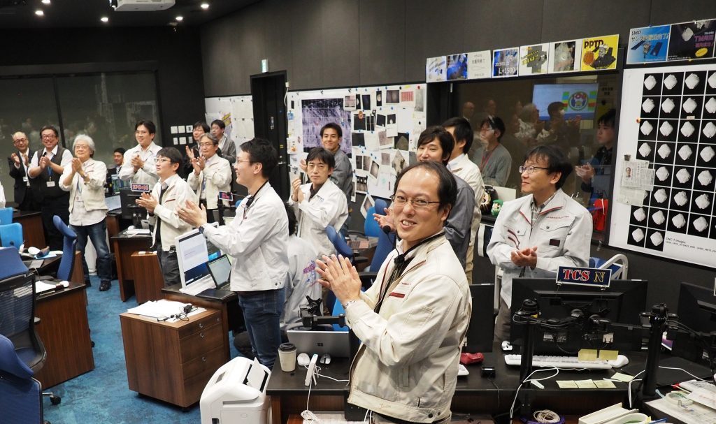 This handout photograph taken and released by the Institute of Space and Astronautical Science of Japan Aerospace Exploration Agency on November 13, 2019 shows Hayabusa2 project manager Yuichi Tsuda (Front) and his colleagues celebrating at the mission control room in Sagamihara city, Kanagawa prefecture. (AFP)