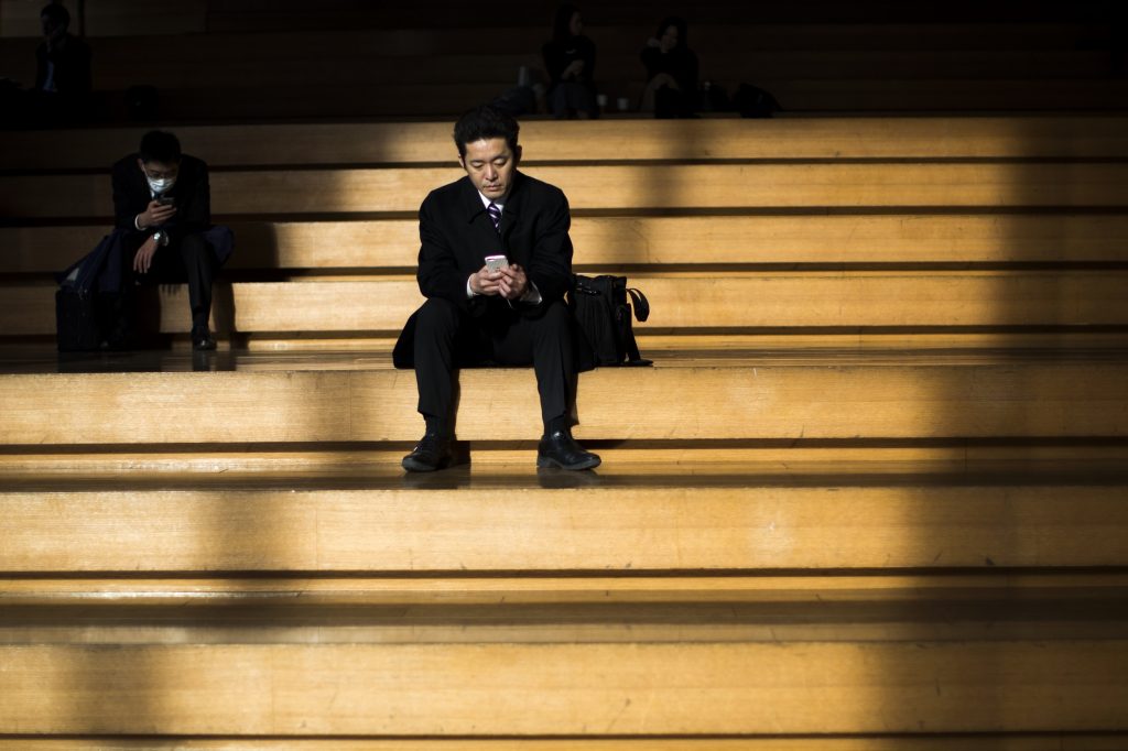 Men check their mobile phones as they take a break from work in the Ginza shopping district in Tokyo on February 13, 2017. (File photo/AFP)