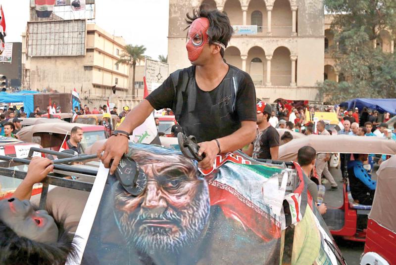 An Iraqi protester hits a poster showing the leader of Iran’s Revolutionary Guard Corps’ Quds Force General Qassem Soleimani with a shoe during anti-government protests in Baghdad. (AP Photo)