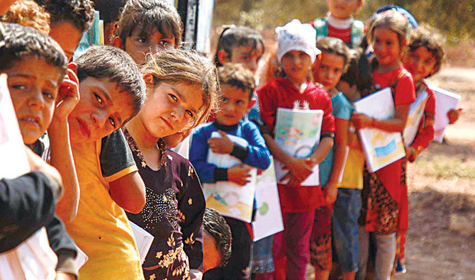 Displaced Syrian children queue outside a bus converted into a classroom in the village of Hazano in northwestern Syria. (AFP)