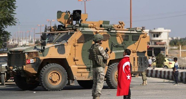 A Syrian boy wearing a Turkish flag stands next to a Turkish soldier in the town of Tal Abyad, Syria. (Reuters)