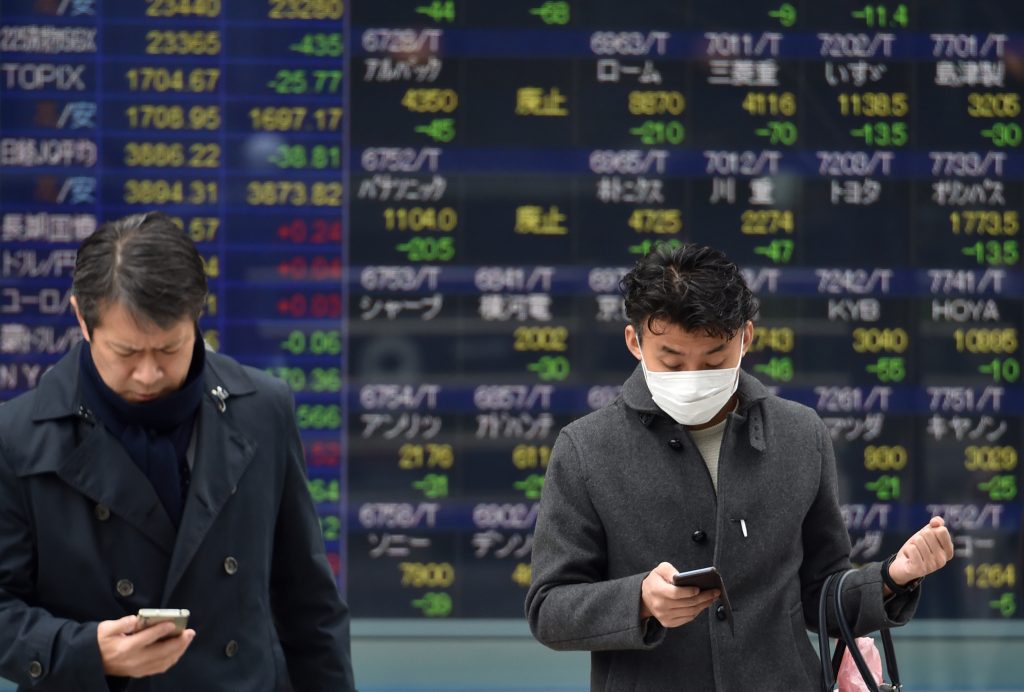 Pedestrians walk in front of an electric quotation board showing stock prices for Japanese companies on the Tokyo Stock Exchange, Tokyo, Jan. 27, 2020. (AFP)