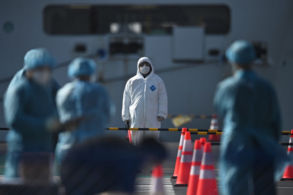 Workers in protective clothes stand before passengers disembarking off the Diamond Princess cruise ship, in quarantine due to fears of new COVID-19 coronavirus, Yokohama, Feb. 21, 2020. (AFP)