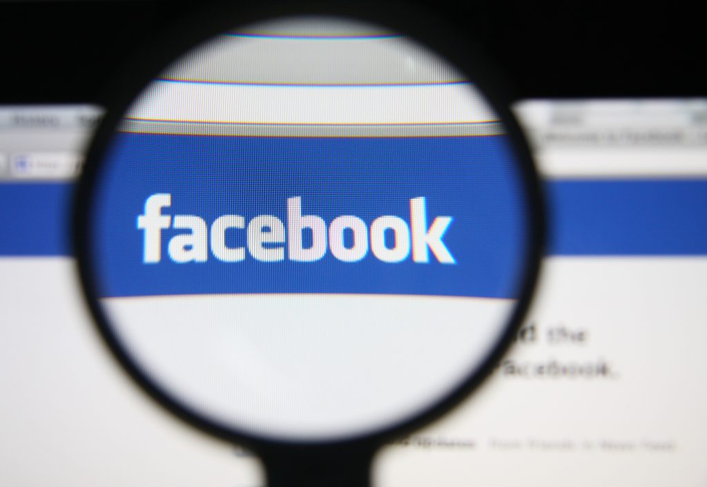 Photo of Facebook homepage on a monitor screen through a magnifying glass. (Shutterstock)