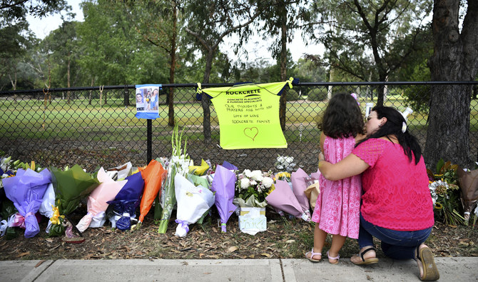 A woman pauses with a young girl near flowers placed at the scene where seven children were hit on a footpath by a four-wheel drive in the Sydney suburb of Oatlands, Sunday, Feb. 2, 2020.  (AP)