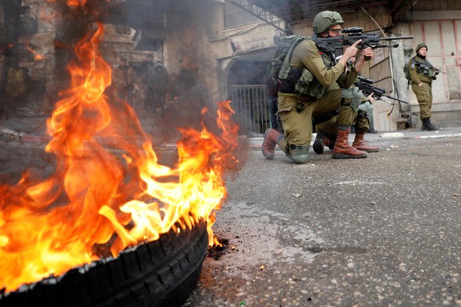 An Israeli soldier aims his weapon as a tire burns during a Palestinian protest against the Middle East peace plan, in Hebron in the Israeli-occupied West Bank Jan. 31, 2020. (Reuters)