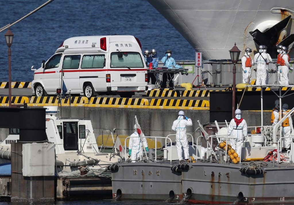Workers in protective gear are seen next to a waiting ambulance at the Japan Coast Guard base in Yokohama on Feb. 5, 2020. (AFP)