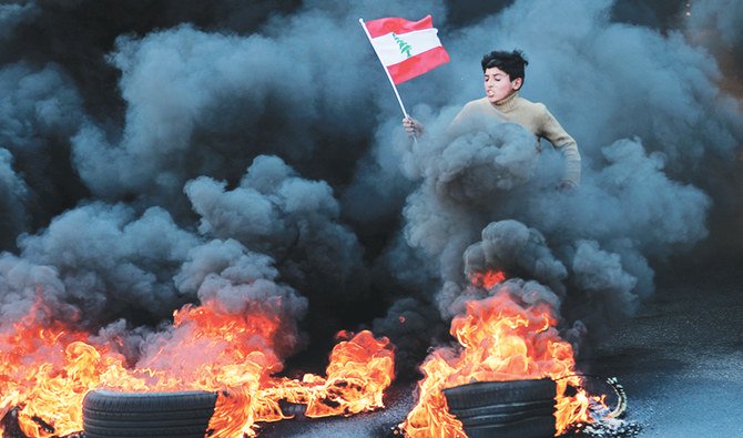 A Lebanese youth runs with a national flag as smoke billows from burning tires during protests that turned into violent riots in Beirut. (AFP)