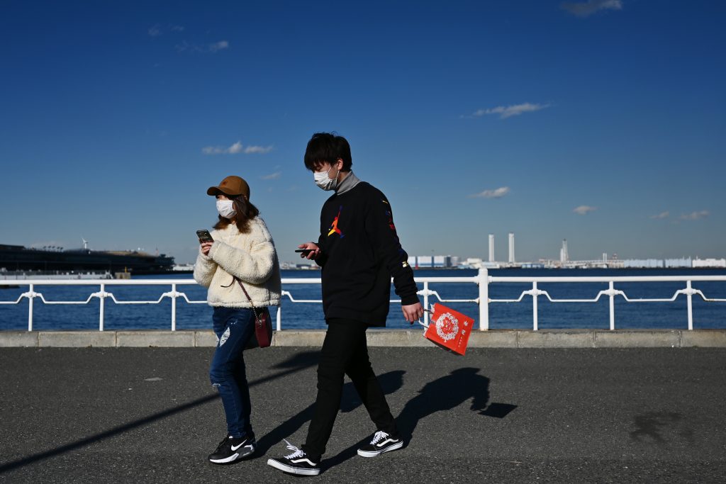 People wearing face masks walk by the coast in Yokohama on Feb. 18, 2020. (AFP)