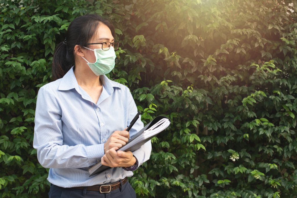 Woman wearing face mask and holding books. (Shutterstock)