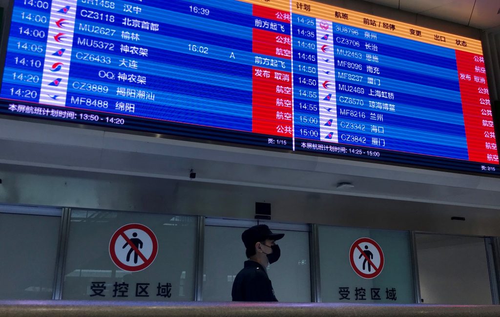 A man wearing a facemask stands under a screen showing mostly cancelled flights at Tianhe airport in Wuhan, China, Jan. 23, 2020. (AFP)
