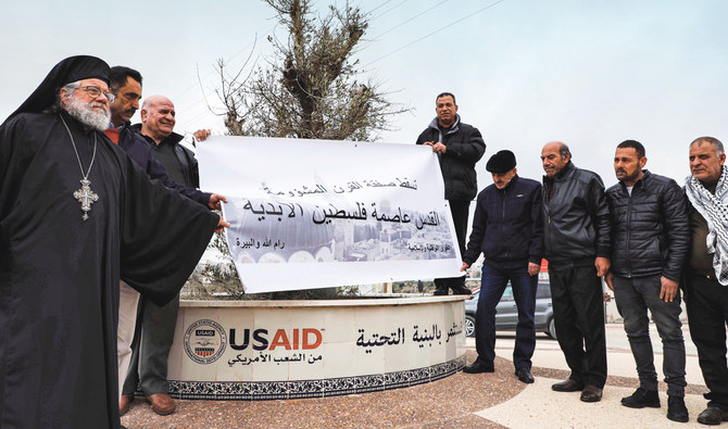 Archimandrite Abdullah Yulio, left, parish priest of the Melkite Greek Catholic church in Ramallah, stands with Palestinian protesters holding up a sign reading in Arabic ‘down with the ominous deal of the century, Jerusalem is the eternal capital of Palestine,’ in the city of Ramallah. (AFP)