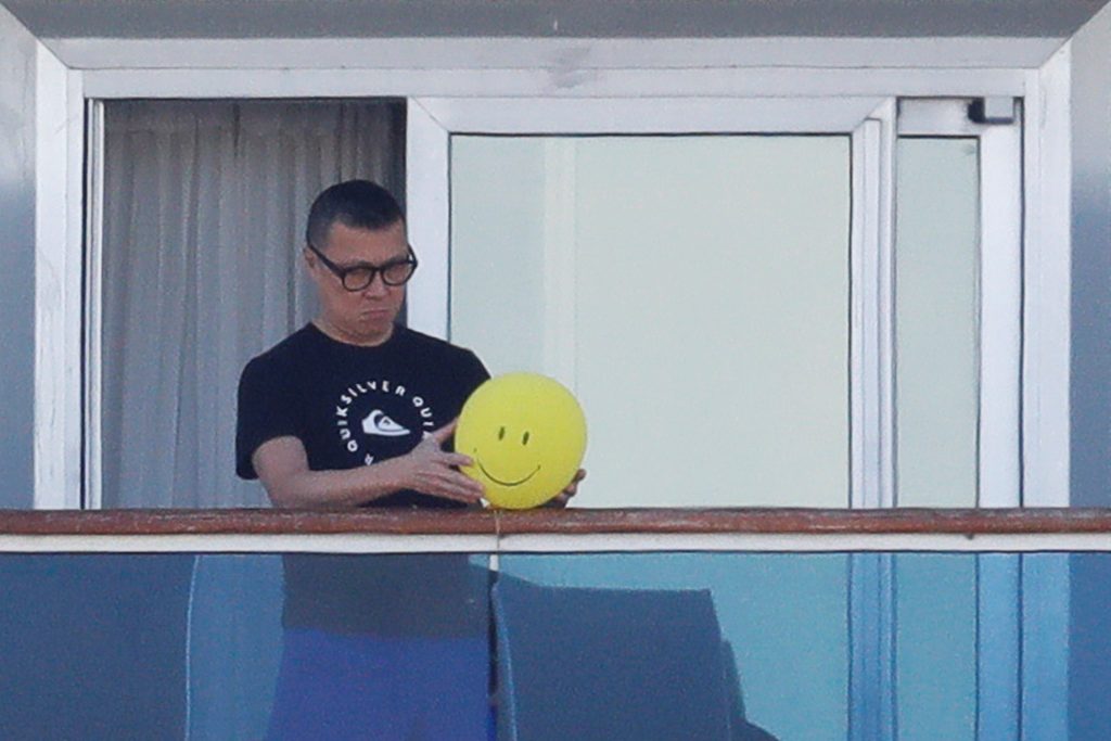 A passenger reacts as he holds a balloon with a smiley face at the balcony of his cabin on the cruise ship Diamond Princess, Feb. 10, 2020. (Reuters)