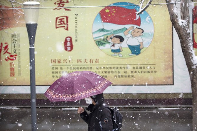 A man wears a face mask as he walks past a propaganda billboard encouraging patriotism during a snowfall in Beijing on Feb. 2, 2020. (AP Photo/Mark Schiefelbein)