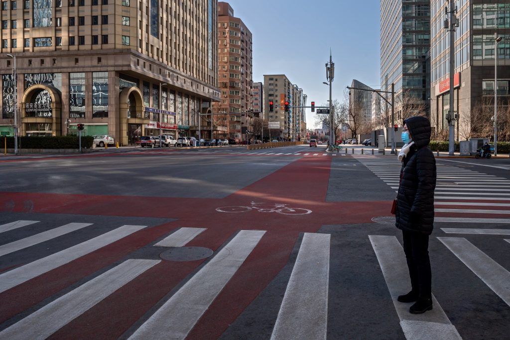 A woman wearing a face mask as a preventive measure against the COVID-19 coronavirus waits to cross a street in the financial district in Beijing on March 3, 2020. (AFP)