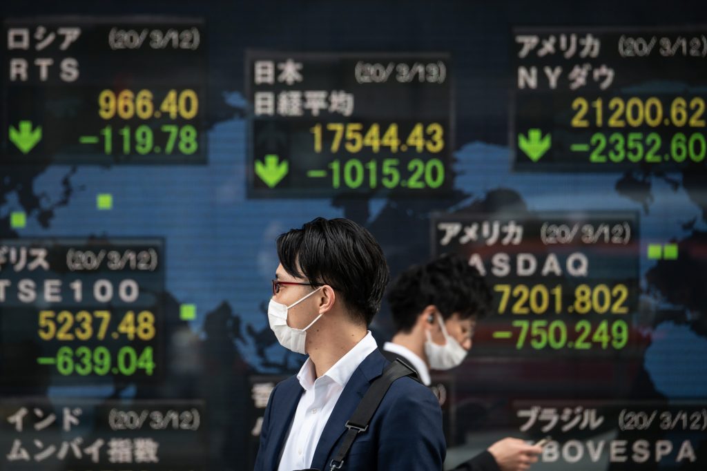 Pedestrians wearing face masks walk past an electric board showing the Nikkei 225 index (C) on the Tokyo Stock Exchange, March. 13, 2020. (AFP)