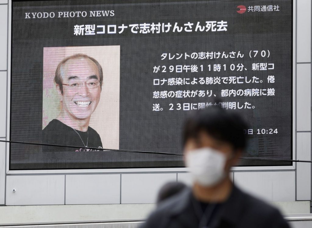 A man wearing a protective face mask, following an outbreak of the coronavirus disease (COVID-19), walks past in front of a huge screen reporting death of Japanese comedian Ken Shimura, who had been hospitalised after being infected with the new coronavirus, in Osaka, western Japan March 30, 2020, in this photo taken by Kyodo. (Kyodo/via REUTERS)