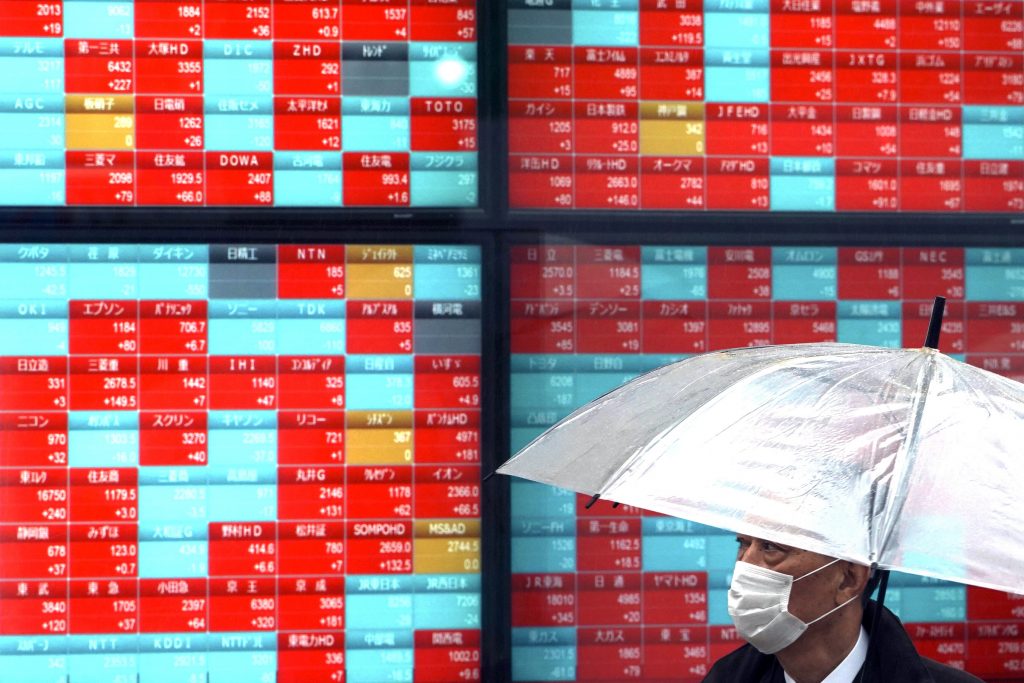 A man with protective mask stands in the rain near an electronic stock board showing Japan's Nikkei 225 index at a securities firm in Tokyo, March. 23, 2020. (AFP)