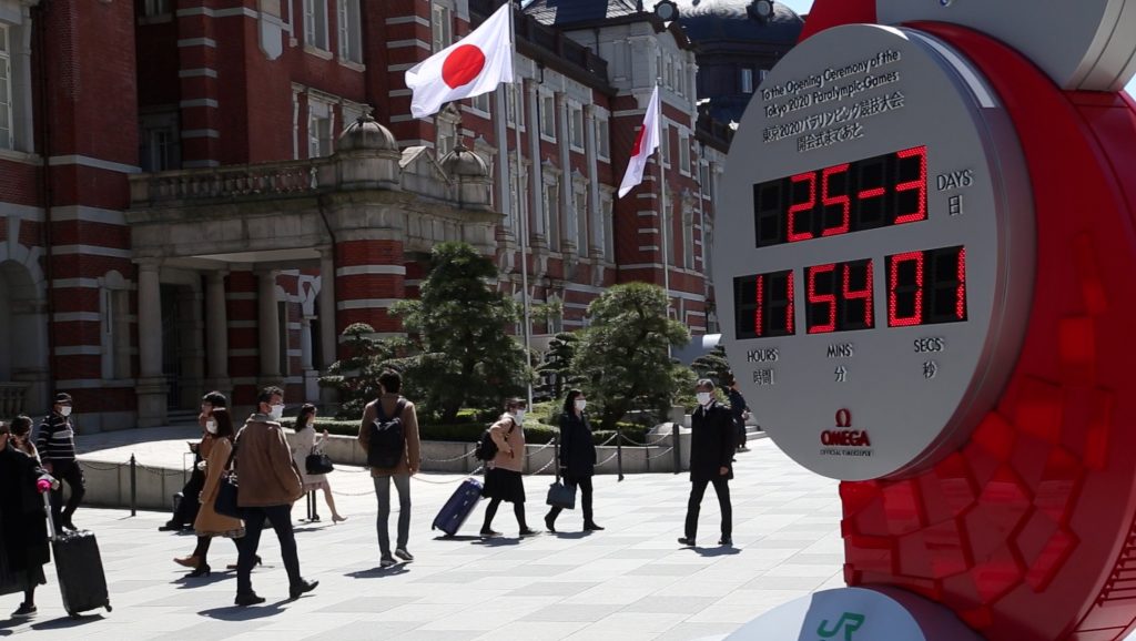 Japanese people with masks on their faces walk past the red and white clock in the Tokyo Station plaza. (AN photo)