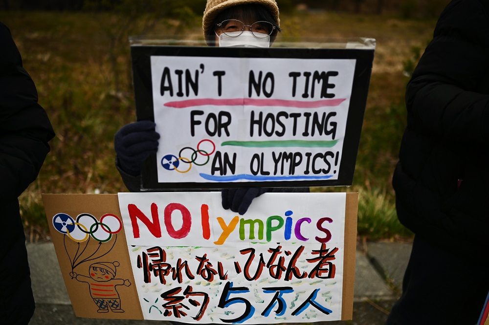 This photo taken on February 29, 2020 shows a protester holding placards during a demonstration against the Olympics, Prime Minister Shinzo Abe and nuclear energy, near the 