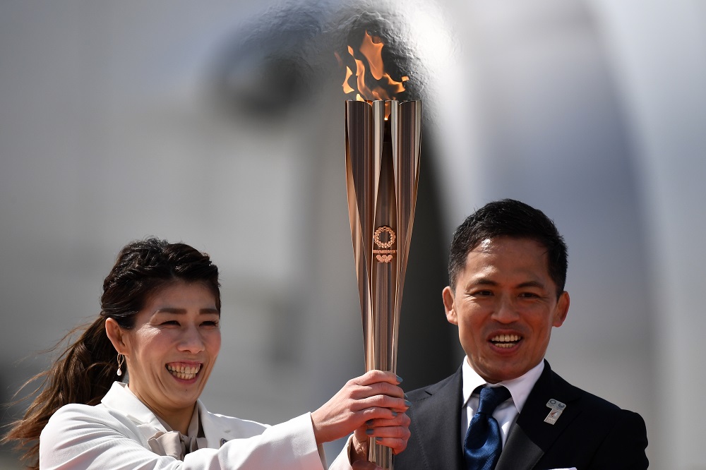 Japanese three-time Olympic gold medallists Saori Yoshida (left) and Tadahiro Nomura hold the Tokyo 2020 Olympic torch at the Japan Air Self-Defense Force Matsushima Base in Higashimatsushima, Miyagi prefecture on March 20, 2020. (AFP)