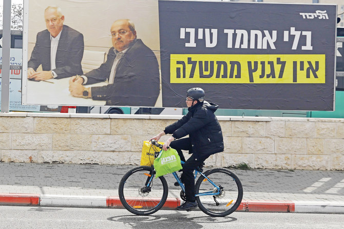 A man rides past an electoral billboard showing the portraits of opposition leader Benny Gantz, left, and Ahmad Tibi, an Arab leader in Jerusalem. (AFP)