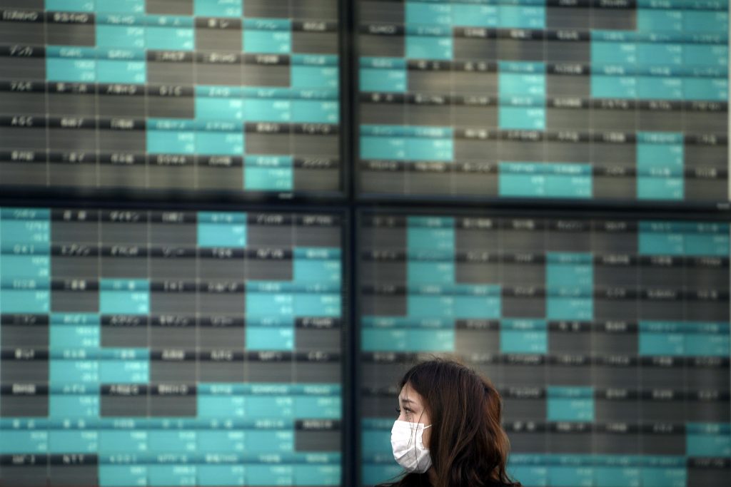 A woman stands in front of an electronic stock board showing Japan's Nikkei 225 index at a securities firm in Tokyo. Asian stock markets and U.S. futures fell Monday, March 16, 2020.