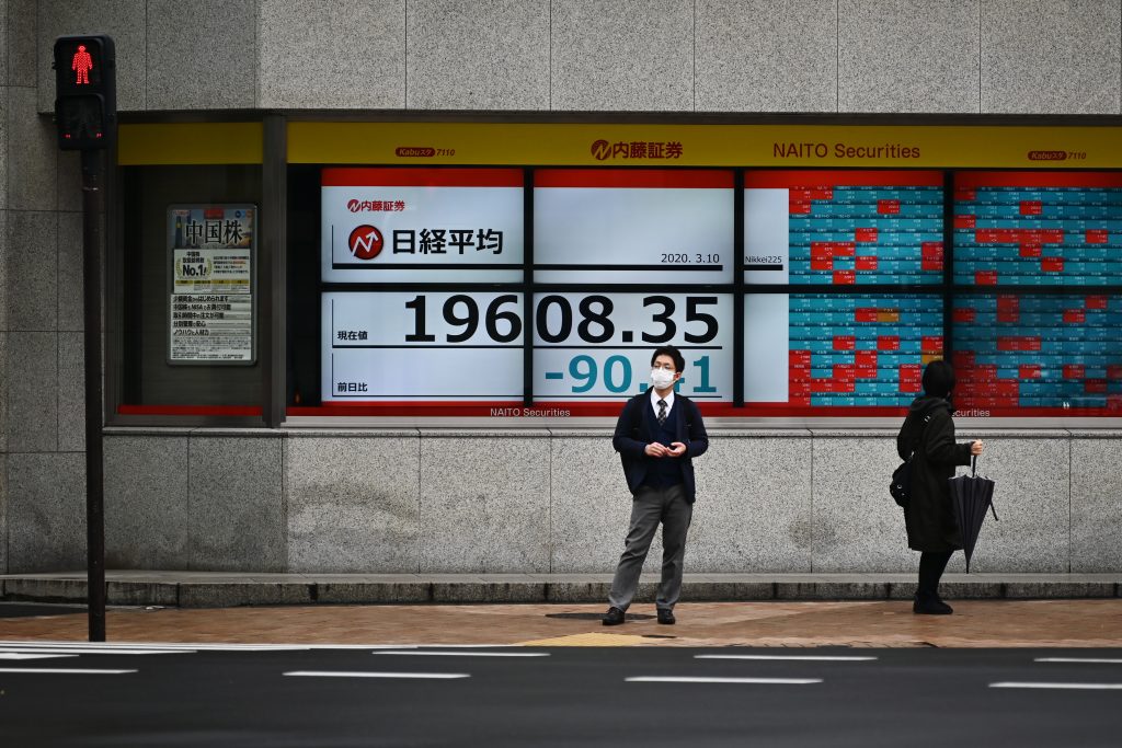 Pedestrian wearing a mask stands in front of a quotation board displaying the share price numbers of the Tokyo Stock Exchange in Tokyo on March 10, 2020.