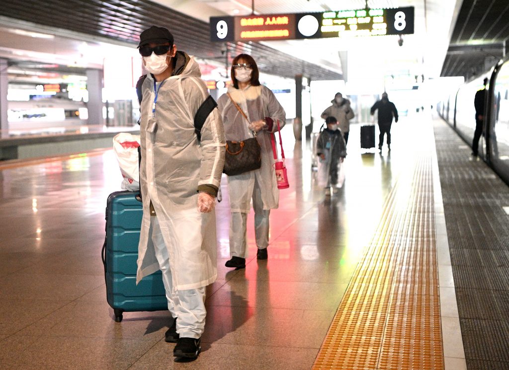 A family wearing facemasks and plastic raincoats walk at the departure area of the Hongqiao railway station in Shanghai on March 2, 2020. (AFP)