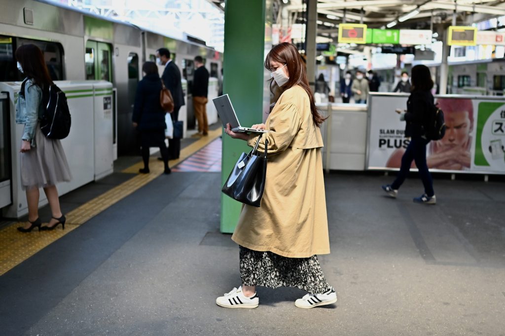A woman works on her laptop computer while entering a train at Gotanda train station in Tokyo on April. 8, 2020. (AFP)
