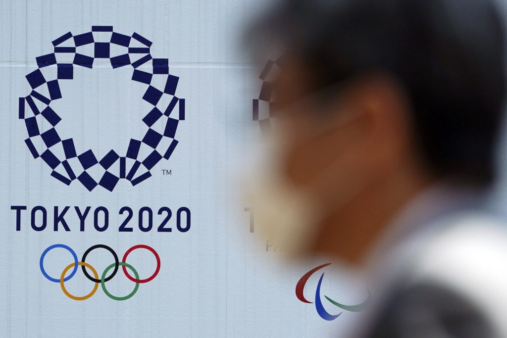 In this April 2, 2020, file photo, a man wearing a face mask walks near the logo of the Tokyo 2020 Olympics, in Tokyo. Tokyo organizers said Tuesday, April 14, 2020 they have no 'Plan B' for again rescheduling the Olympics, which were postponed until next year by the virus pandemic. They say they are going forward under the assumption the Olympics will open on July 23, 2021. (AP) 