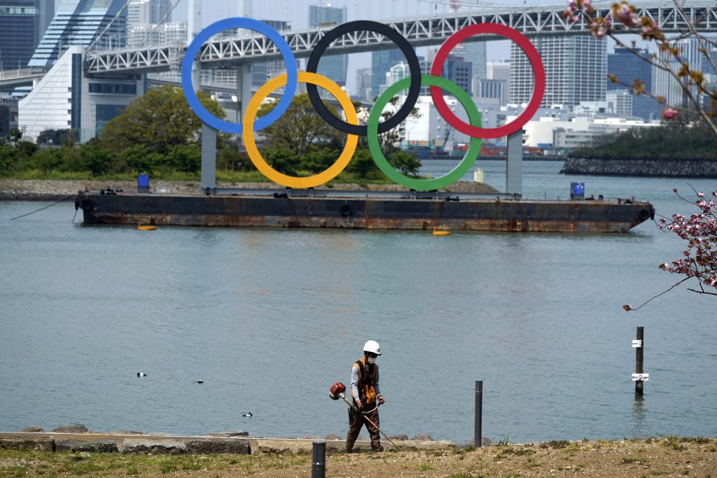 A worker operates a mowing machine near the Olympic rings at Tokyo's Odaiba district Thursday, April 16, 2020, in Tokyo. Japanese Prime Minister Shinzo Abe declared a state of emergency last week for Tokyo and some other prefectures to ramp up defenses against the spread of the coronavirus. (AP Photo)