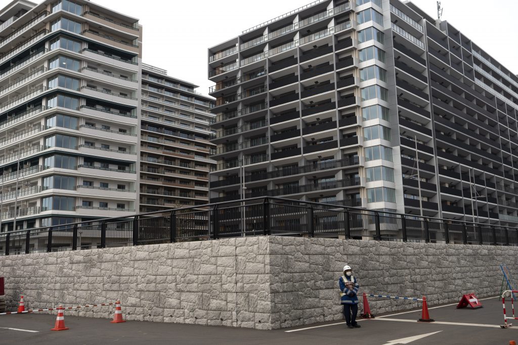 In this March 23, 2020, file photo, a guard stands in front of apartment buildings at the athletes' village for the Tokyo 2020 Olympics in Tokyo. A group representing the homeless is asking to use the Athletes Village for next yearâ€™s Tokyo Olympics as a shelter during the coronavirus pandemic. An online petition addressed to Tokyo Olympic organizers and the city government has drawn ten of thousands of signatures for permission to occupy the massive housing complex going up alongside Tokyo Bay. (AP Photo)