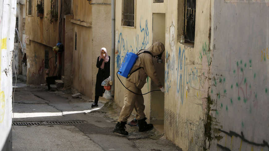 A Palestinian woman covers her face with her scarf as a civil defense worker disinfects the streets of Aida refugee camp, in the West Bank. (AFP)