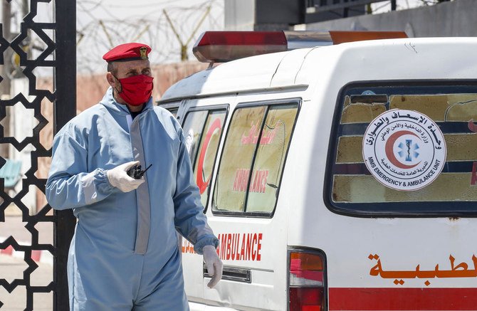 An ambulance drives past a member of the security forces loyal Gaza's Islamist rulers Hamas, wearing personal protective equipment as a precaution against the coronavirus (COVID-19) pandemic, at the Rafah border crossing with Egypt, in the southern Gaza Strip on April 13, 2020, after the crossing was temporarily reopened for four days. (AFP)