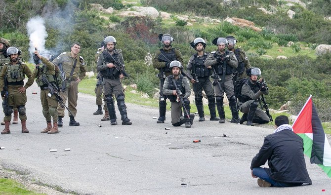 A man holding a Palestinian flag stages a sit-in opposite members of the Israeli border police clashing with Palestinians protesting Israeli settlements and a controversial US-brokered peace plan, in the Jordan Valley area of the occupied West Bank, on February 25, 2020. (AFP)