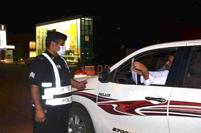 A motorist shows to a Saudi police officer a document allowing him to travel during curfew hours. (SPA)