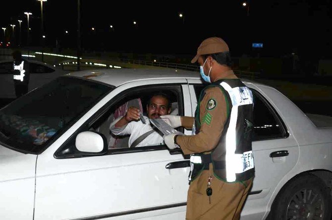 A motorist shows to a Saudi police officer a document allowing him to travel during curfew hours. (SPA)