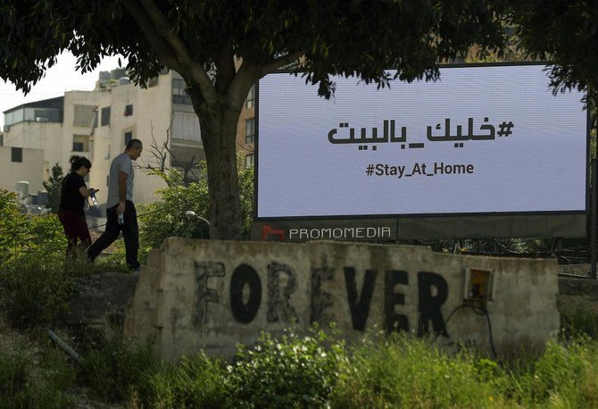 Pedestrians walk behind a billboard calling residents to stay at home in Beirut's downtown district, during the coronavirus pandemic crisis, on April 19, 2020. (AFP)
