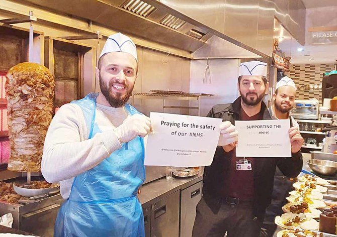 Hiba Express staff holding signs of support for the UK’s National Health Service as they prepare food for its workers. (Supplied)