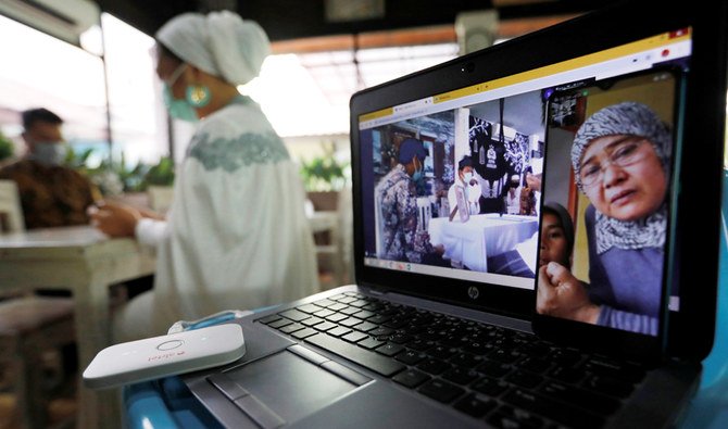 Family members are seen on a computer screen showing video conference as the bride Ugi Lestari Widya Bahri prays in the backround, during a wedding ceremony which streamed online amid the spread of coronavirus disease (COVID-19), in Tangerang, on the outskirts of Jakarta, Indonesia, April 10, 2020. (REUTERS)